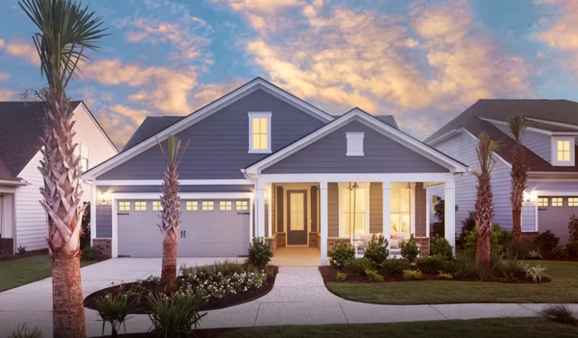 A single-story Del Webb home at dusk, with palm trees lit up in front.