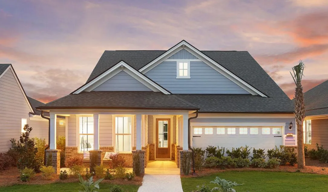 Una casa de Del Webb de una planta al anochecer, con las palmeras iluminadas.