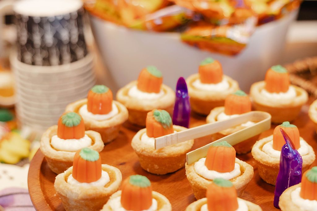 Mini tarts topped with candy pumpkins on a wooden serving tray Mini tarts topped with candy pumpkins on a wooden serving tray