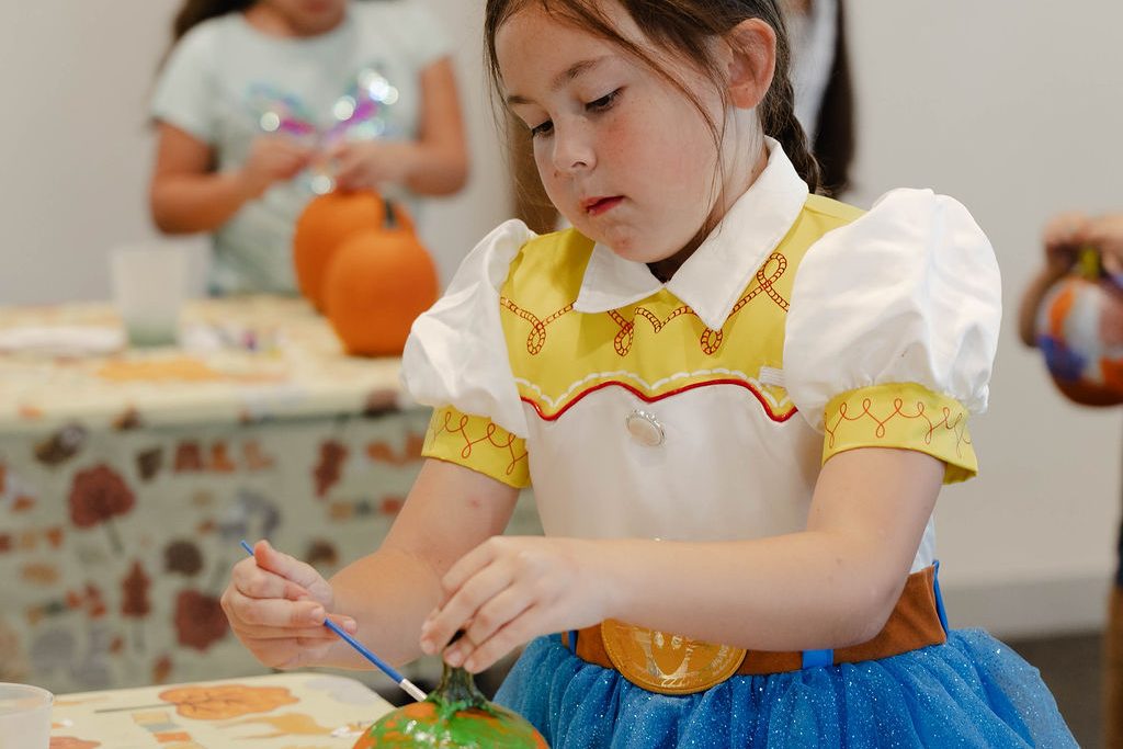 Girl in a cowgirl costume painting a small pumpkin Girl in a cowgirl costume painting a small pumpkin