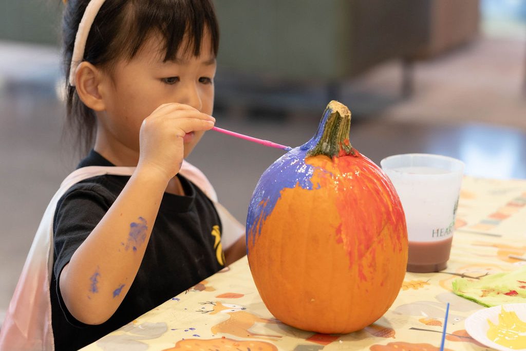 Girl in a unicorn headband painting an orange and purple pumpkin Girl in a unicorn headband painting an orange and purple pumpkin